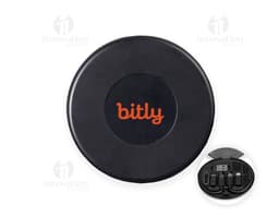 Puck de metal preto brilhante com símbolos de seta, círculos e botões, representando um Kit Cabo USB-C com 3 Adaptadores.
