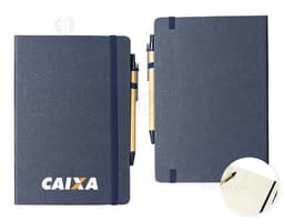 Caderneta de fibra de arroz com caneta em fundo branco. O caderno é marrom claro e possui detalhes em preto na capa. A caneta