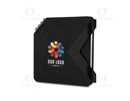 Mini caderno preto de couro aberto sobre uma mesa de escritório, ao lado de um notebook e diversos dispositivos eletrônicos.
