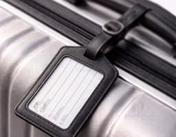 Identificador de Bagagem preto feito de couro, com fecho e interior vazio para inserir informações. Com design compacto e