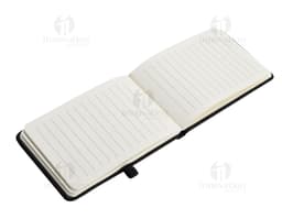 Mini Caderno marrom de couro, aberto, com página em branco. Ao lado, um pen drive, um chaveiro, um diário preto e um celular.