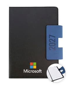 Notebook preto aberto, com teclado e tela exibindo ícones e botões. Ao lado, uma agenda A5 com capa dura em PU, destacando-se contra um fundo preto.