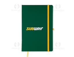 Notebook amarelo aberto com papel pautado em um escritório, ao lado de um modem, um telefone e um copo de bebida.