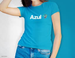 Camiseta feminina de corte cinturado em cor azul, usada por uma modelo sorridente e atraente. Ela está posando de forma