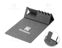 Mouse pad de couro marrom aberto em cima de uma mesa de escritório, ao redor estão um notebook preto, uma bolsa de couro