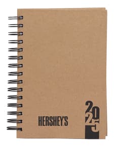 Foto de uma agenda diária para o ano de 2025, com capa marrom e textura de papel antigo. A agenda possui espiral, páginas em