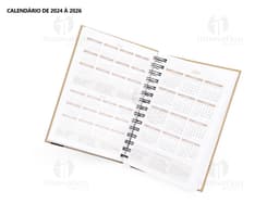 Foto de uma agenda diária para o ano de 2025, com capa marrom e textura de papel antigo. A agenda possui espiral, páginas em