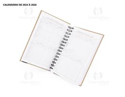 Foto de uma agenda diária para o ano de 2025, com capa marrom e textura de papel antigo. A agenda possui espiral, páginas em