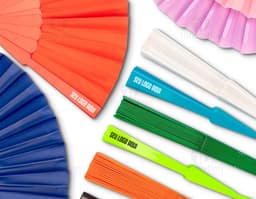 Leque de plástico colorido, com design moderno e brilhante. O leque possui formas geométricas em tons de amarelo, laranja